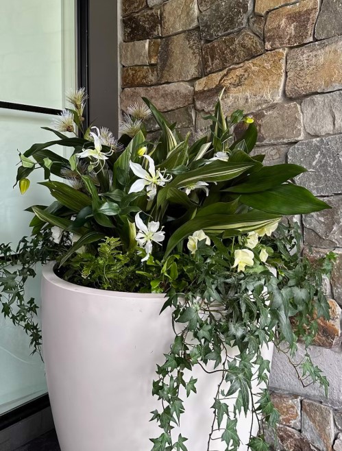 Faux white flowers blending with live plants in shade container planting